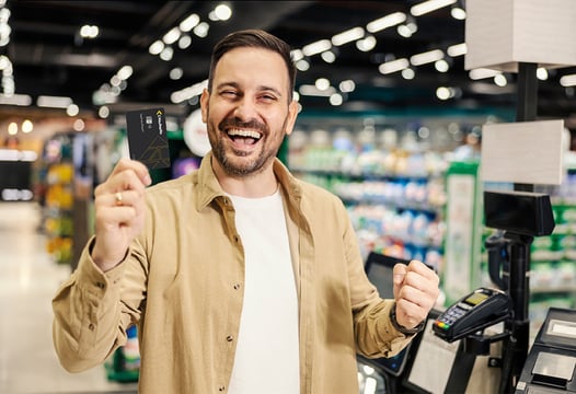 Hombre feliz sosteniendo con su mano su tarjeta de afiliación de Colsubsidio en un establecimiento comercial 